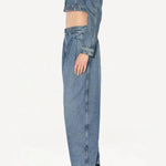 Side view of bleu delave pleated pants on model wearing crop jacket and boots, against a white background.