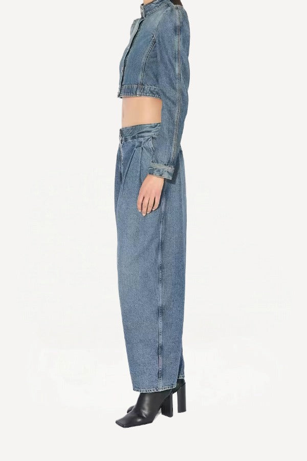 Side view of bleu delave pleated pants on model wearing crop jacket and boots, against a white background.