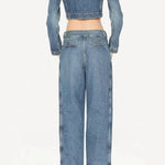 Back view of bleu delave pleated pants on model wearing crop jacket and boots, against a white background.