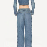 Back view of bleu delave pleated pants on model wearing crop jacket and boots, against a white background.