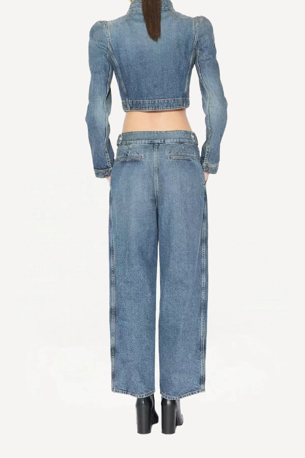 Back view of bleu delave pleated pants on model wearing crop jacket and boots, against a white background.