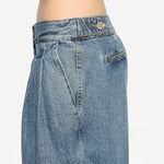 Side closeup view of bleu delave pleated pants on model wearing crop jacket, against a white background.