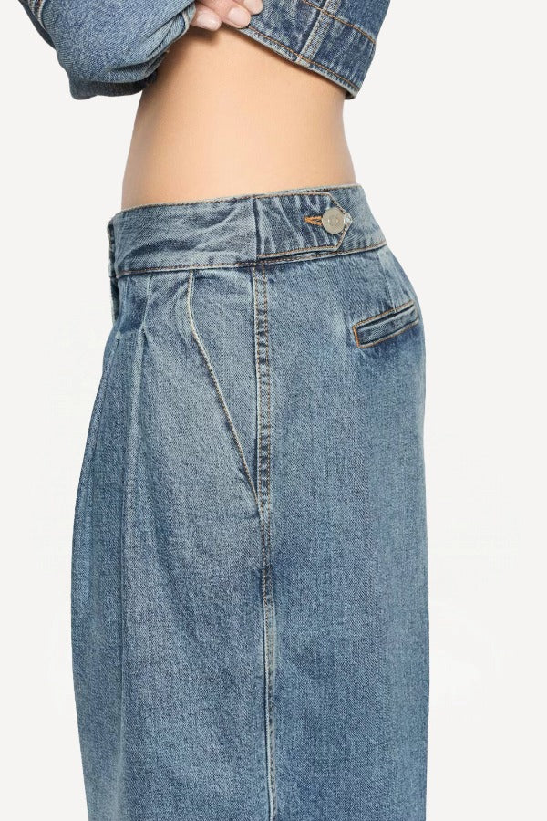 Side closeup view of bleu delave pleated pants on model wearing crop jacket, against a white background.