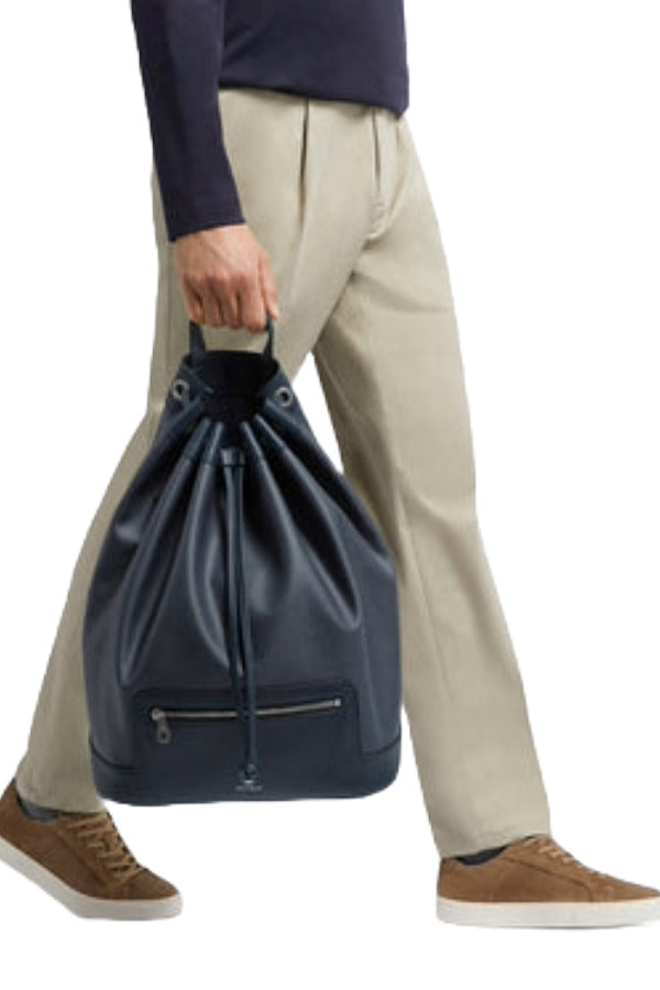 Front view of navy newport shoulder bag on model wearing khaki trousers, a navy sweater and brown sneakers, against a white background.