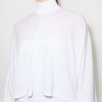 Front closeup view of white batwing jumper on model wearing a white maxi dress underneath, against a white background.