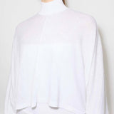 Front closeup view of white batwing jumper on model wearing a white maxi dress underneath, against a white background.