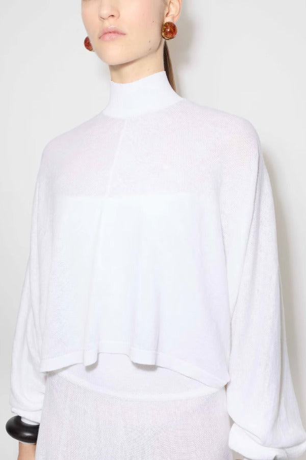 Front closeup view of white batwing jumper on model wearing a white maxi dress underneath, against a white background.