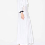 Side view of white linen maxi dress on model wearing white pullover and natural wedges, against white background.