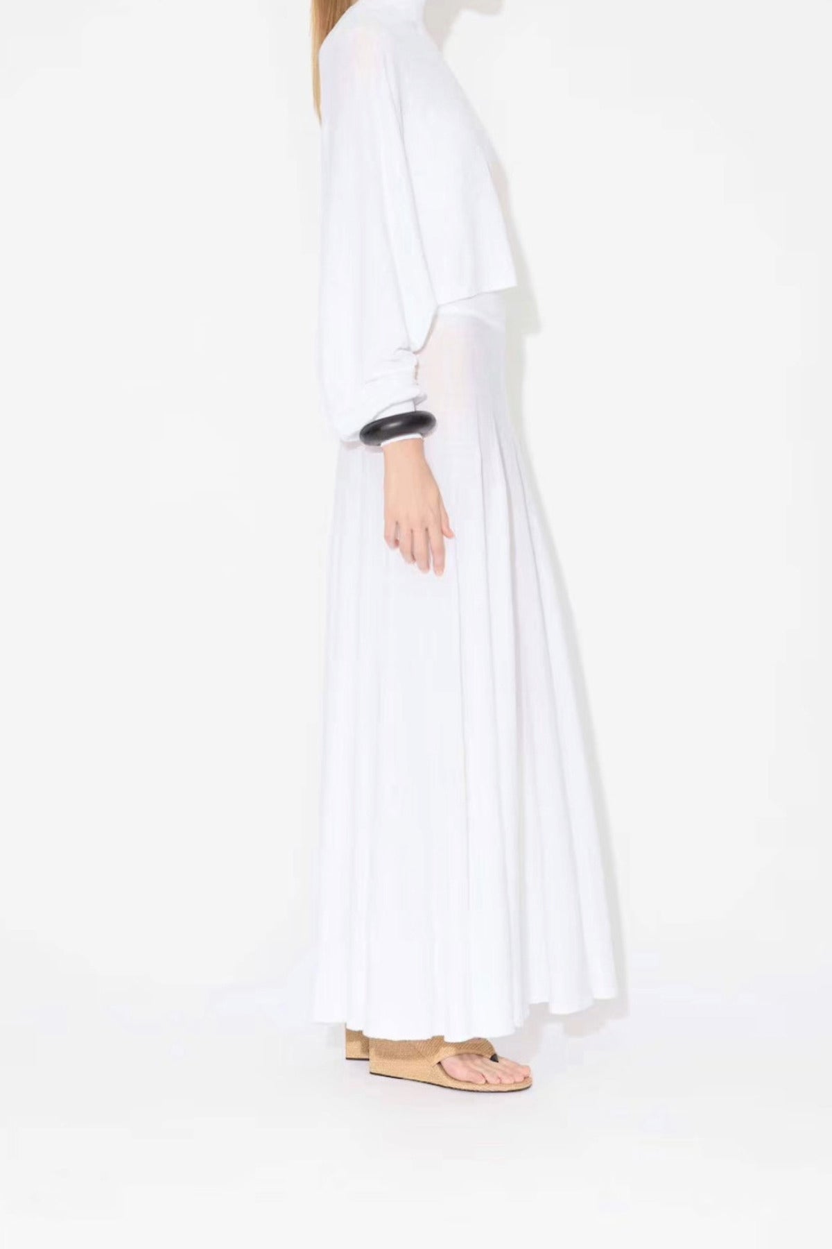 Side view of white linen maxi dress on model wearing white pullover and natural wedges, against white background.
