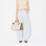 Front view of light blue denim pants with model wearing knotted white top and square ballet flats with brown and creme handbag on white background.