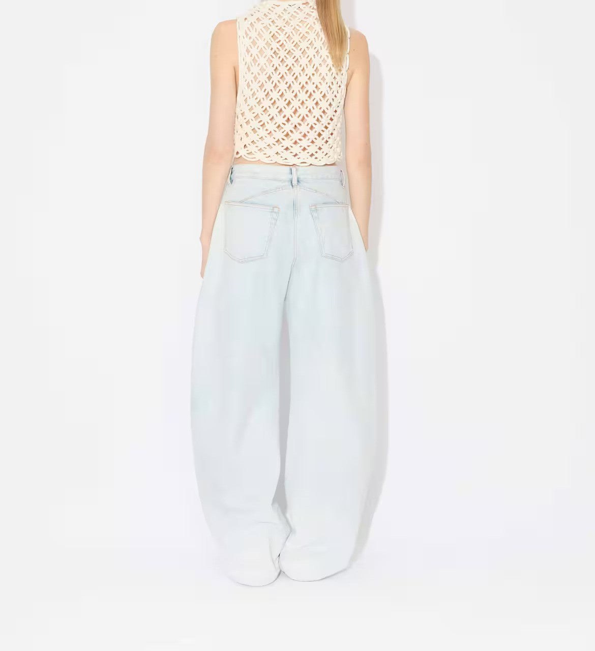 Back view of light blue denim pants on model wearing knotted white top on white background.
