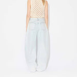 Back view of light blue denim pants on model wearing knotted white top on white background.