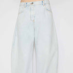 Front closeup view of light blue denim pants on model wearing knotted white top on white background.