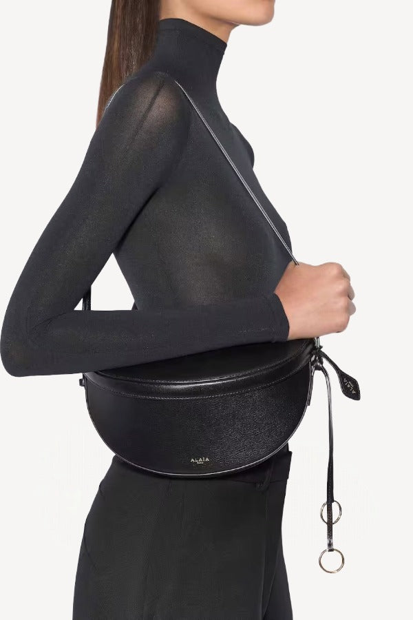 Front view of noir hip east west bag on model wearing black top and pants, against a white background.