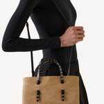 Front view of natural straw bag on model wearing a black short and black skirt on white background.