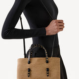 Front view of natural straw bag on model wearing a black short and black skirt on white background.