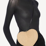 Front view of the natural heart bag in straw on a model wearing black top and black pants on a white background.