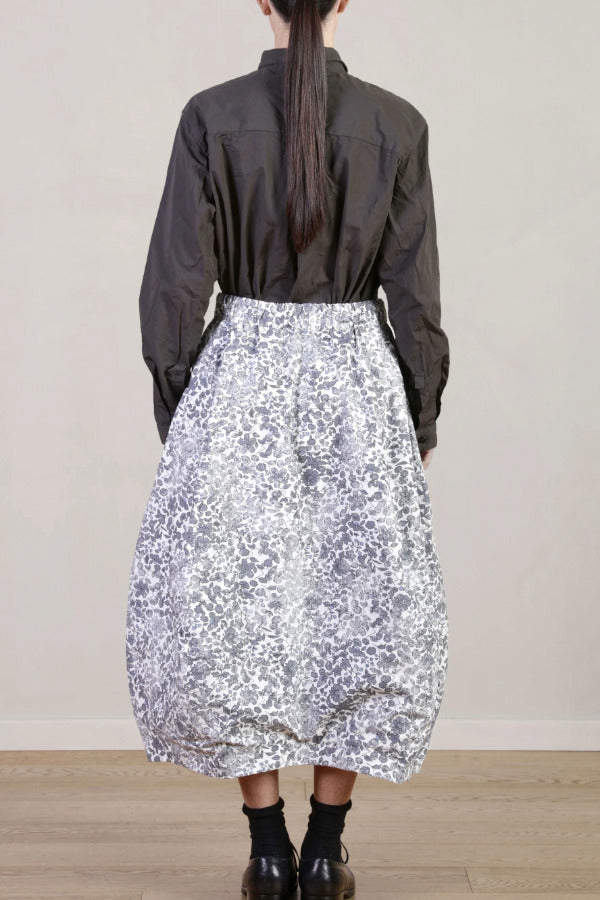 Back view of bright flower carla skirt on model wearing dark grey top with black oxfords, against a white background.