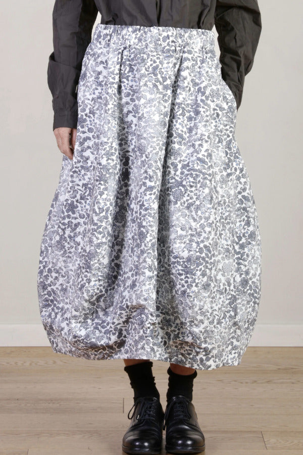 Front closeup view of bright flower carla skirt on model wearing dark grey top with black oxfords, against a white background.