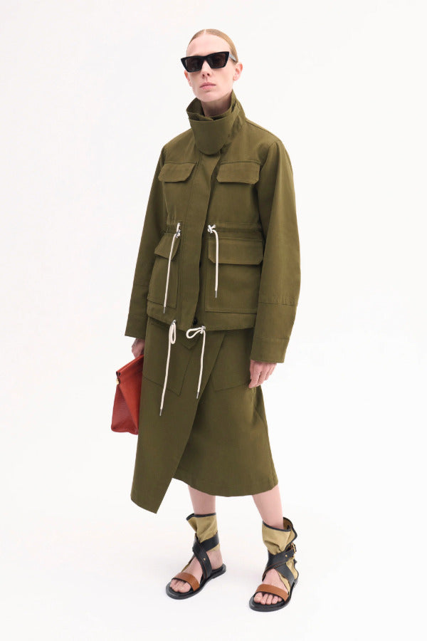 Overhead view of ecru gladiator wrap sandal on model wearing olive jacket and skirt against a white background