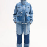 Front view of cropped military jacket on model wearing patchwork denim pants and black sandals on white background.