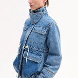 Side Closeup view of cropped military jacket on model wearing denim patchwork pants on white background.