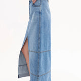 Side view of indigo denim skirt on model wearing black tank top and black sandals, against a white background.