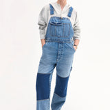 Front view of indigo overalls on model wearing grey hoodie and black sandals, against white background.