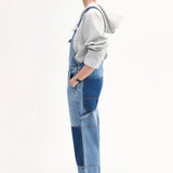 Side view of indigo overalls on model wearing grey hoodie and black sandals on white background