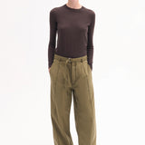 Front view of olive drop waist pant on model wearing brown long-sleeve t-shirt and pointed toe heels on white background.