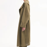 Side view of olive oversized trench coat mo model wearing brown shirt, olive trousers and black pointed toe heels on white background