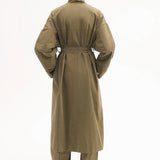 Back view of olive oversized trench coat on model wearing olive pants and black pointed toe heels on white background.