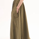 Side view of olive parachute skirt on model wearing dark green tank top and black sandals, against white background.