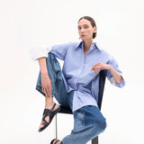 A model with light brown hair is shown in the black leather shoes sitting in a chair grabbing her knee to show the shoe with a white background.