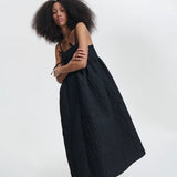 Side view of black ambra dress on model wearing black sneakers, against a white background.