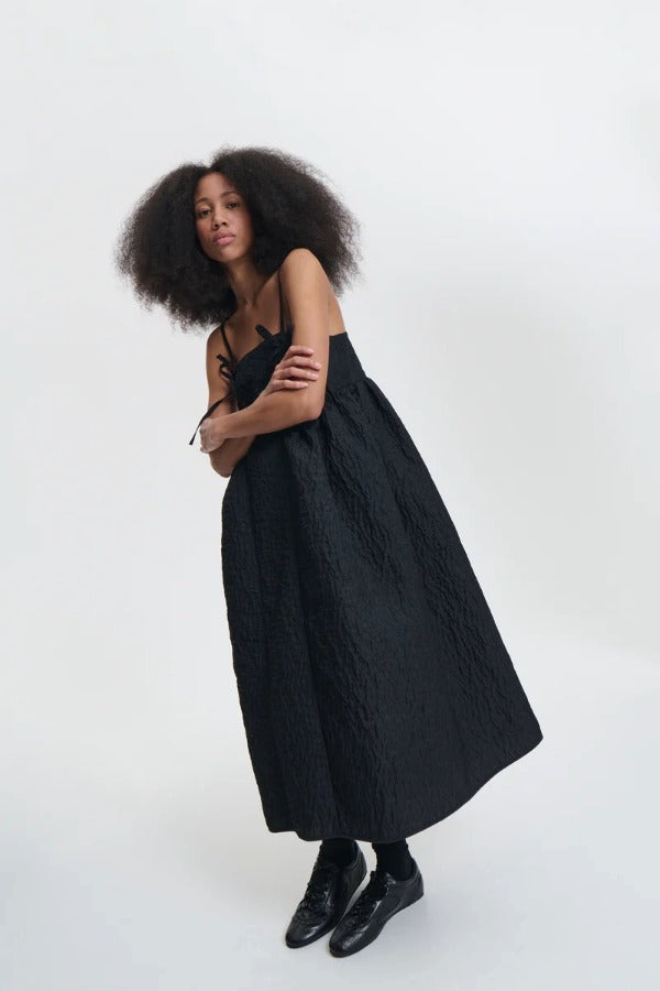 Side view of black ambra dress on model wearing black sneakers, against a white background.