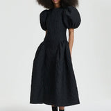 Front view of black bali dress on model wearing black sneakers and socks, against a white background.