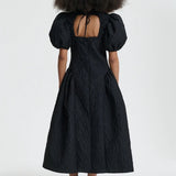 Back view of black bali dress on model wearing black sneakers and socks, against a white background.