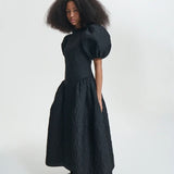 Side view of black bali dress on model wearing black sneakers and socks, against a white background.