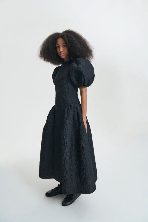 Side view of black bali dress on model wearing black sneakers and socks, against a white background.