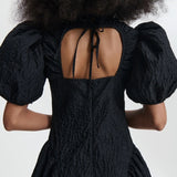 Back closeup view of black bali dress on model, against a white background.