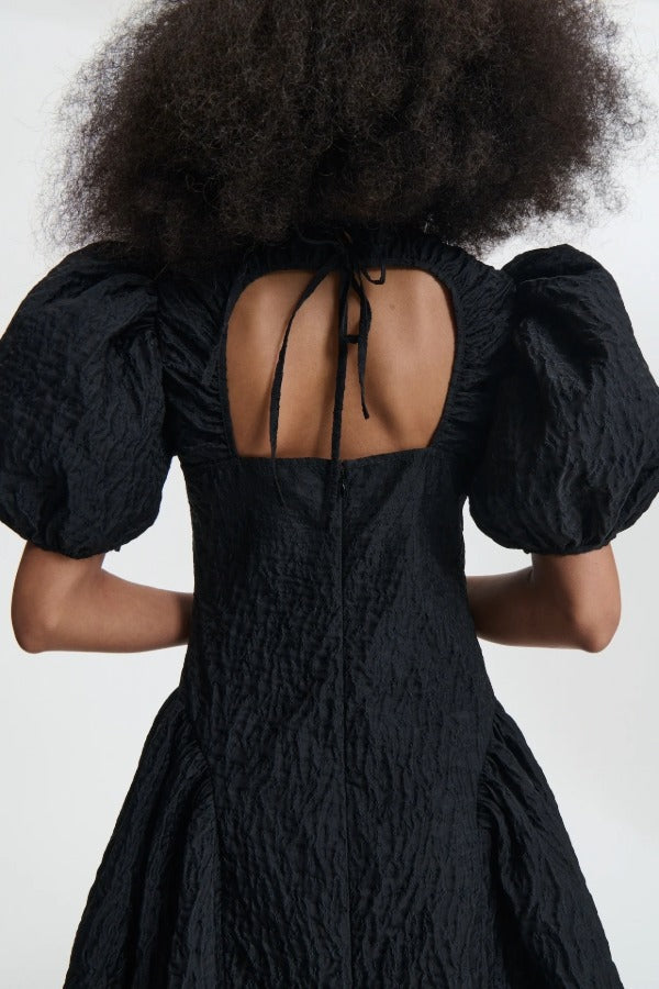 Back closeup view of black bali dress on model, against a white background.