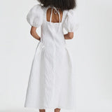 Back view of white bali dress on model wearing black flats, against a white background.