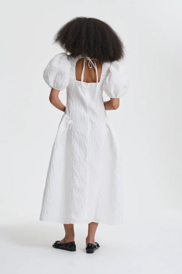 Back view of white bali dress on model wearing black flats, against a white background.