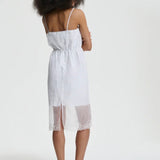 Back view of white barr dress on model wearing black flats, against a white background.