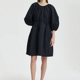 Front view of black birgitte dress on model wearing black flats, against a white background.
