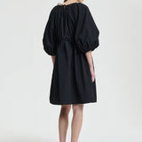 Back view of black birgitte dress on model wearing black flats, against a white background.