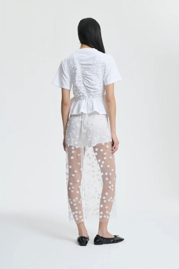 Back view of gus skirt on model wearing white shorts and top with flats, against a white background.
