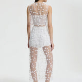 Back view of white utania top on model wearing white shorts and black flats, against a white background.