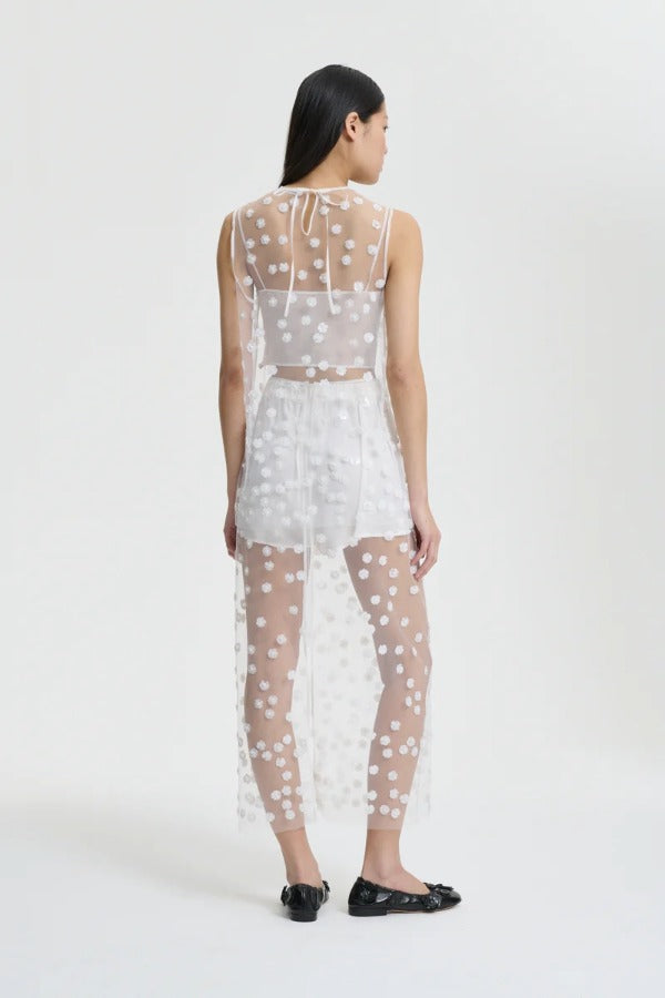 Back view of white utania top on model wearing white shorts and black flats, against a white background.